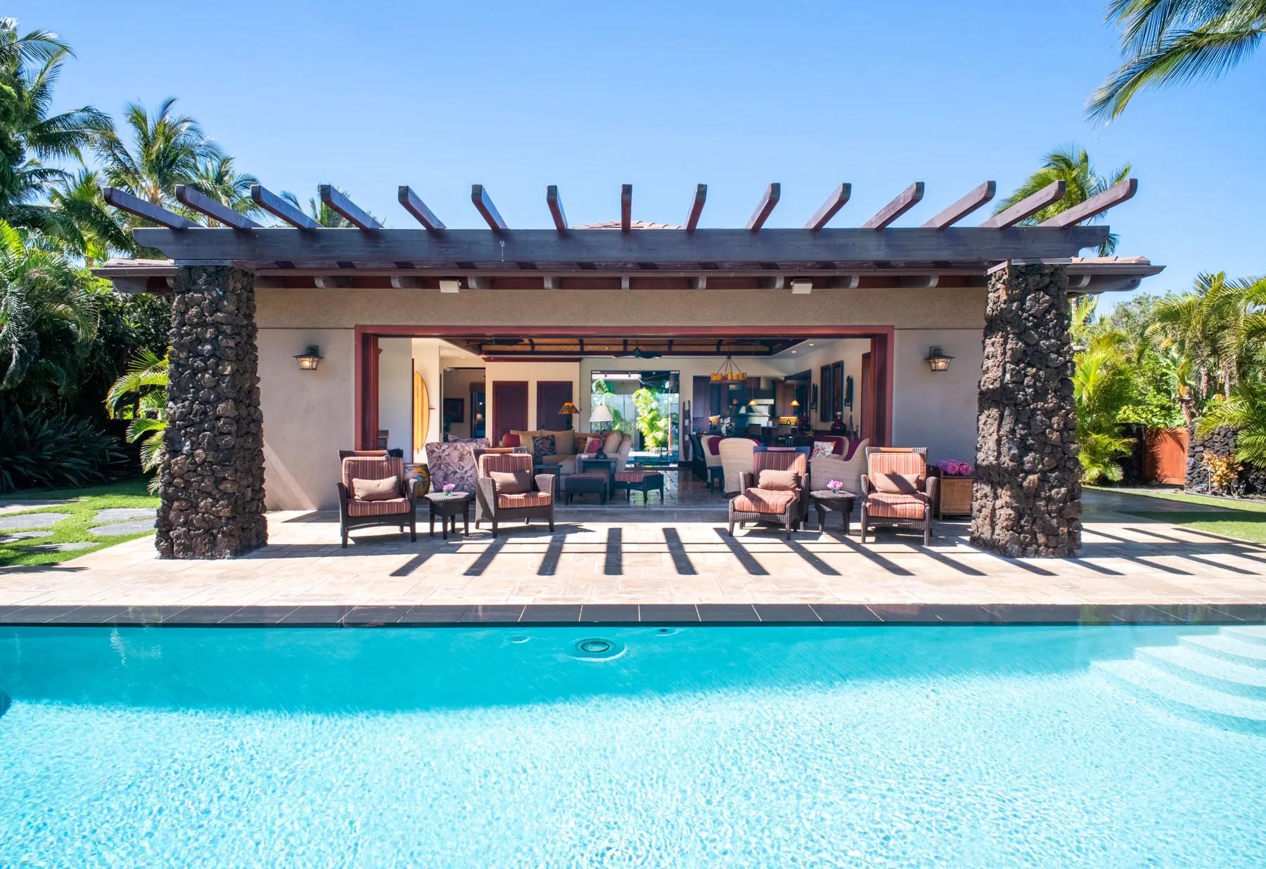 A poolside patio with outdoor seating beneath a pergola.