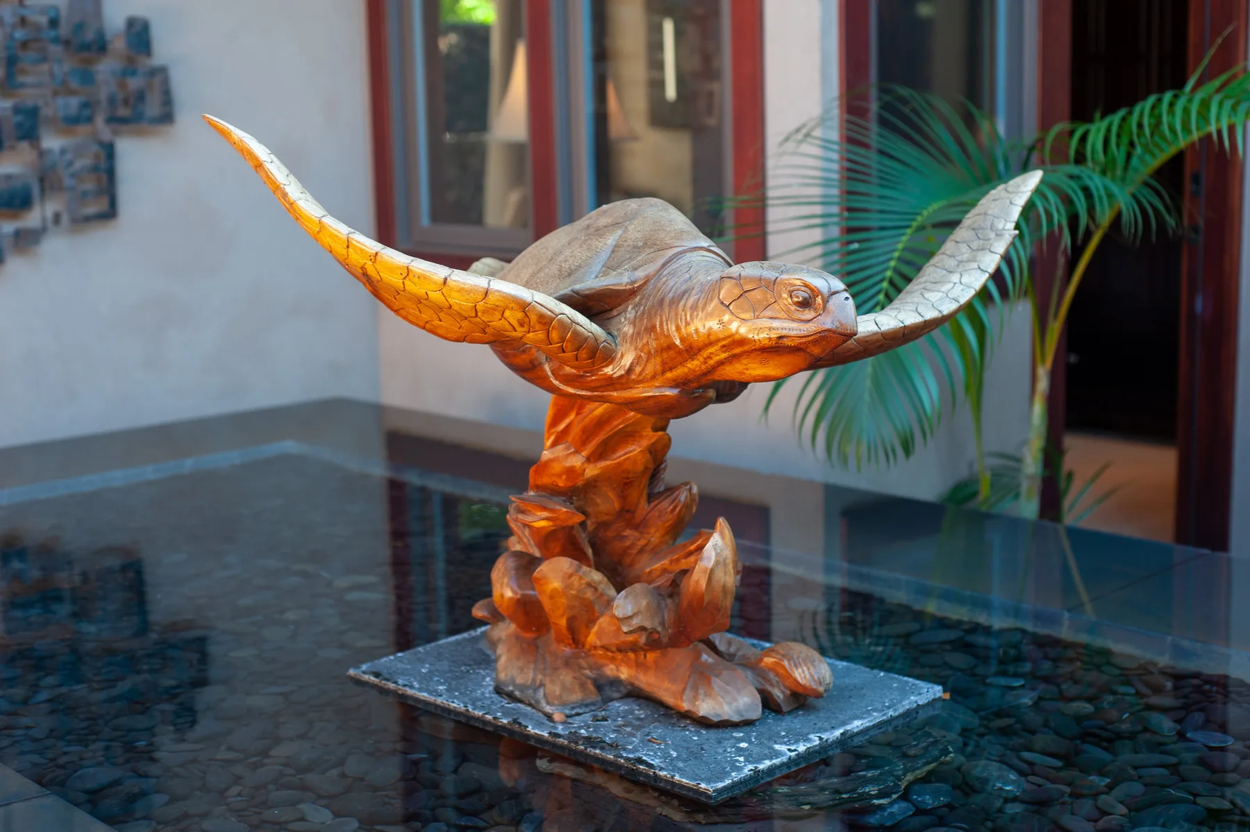 A carved sea turtle sculpture stands on a stone base in an indoor display area.