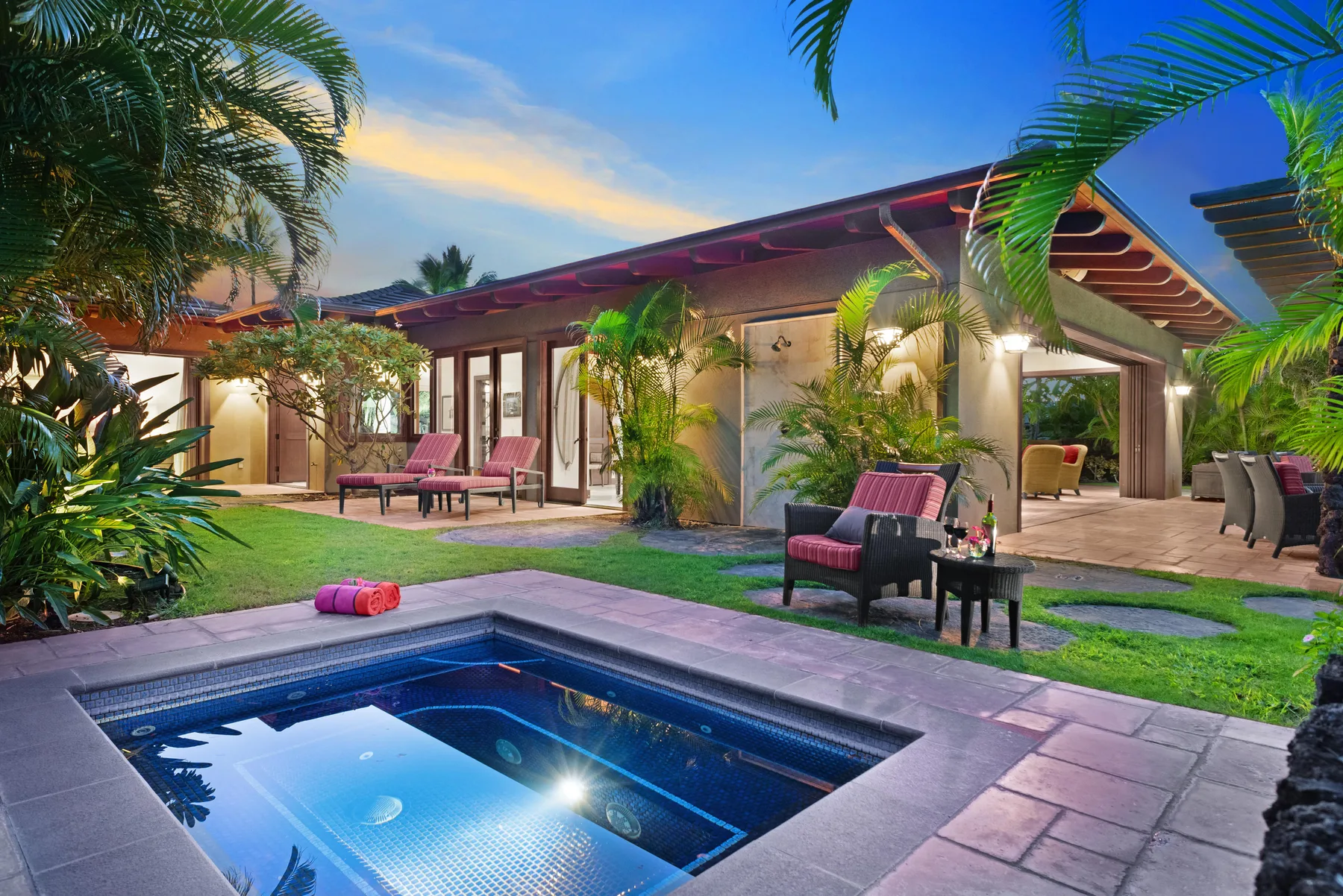 A tropical outdoor pool sits beside a modern house and patio seating.
