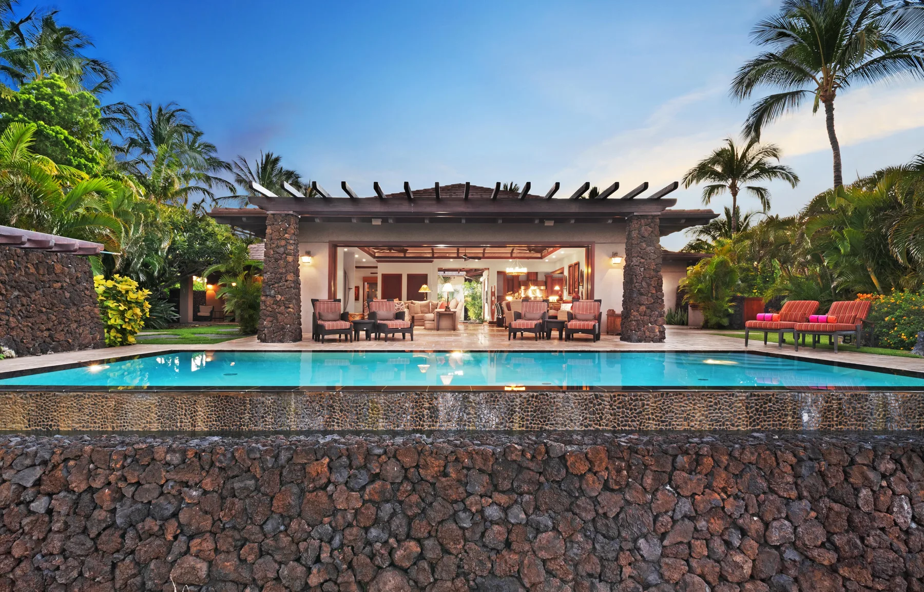 An open-air dining area overlooks a swimming pool, with tropical greenery around it.