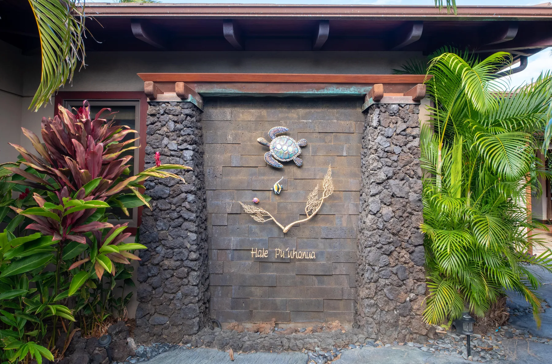 A stone entrance wall features a turtle ornament and tropical plants.