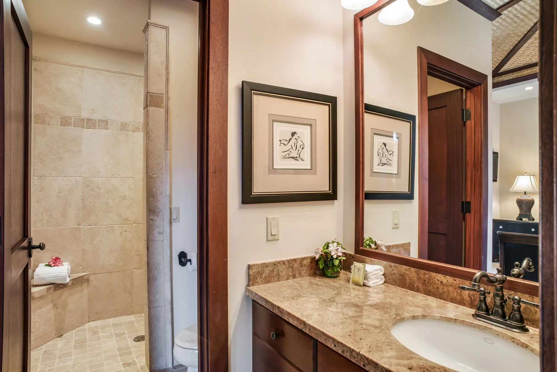 A bathroom vanity with a sink and a framed print beside the shower.