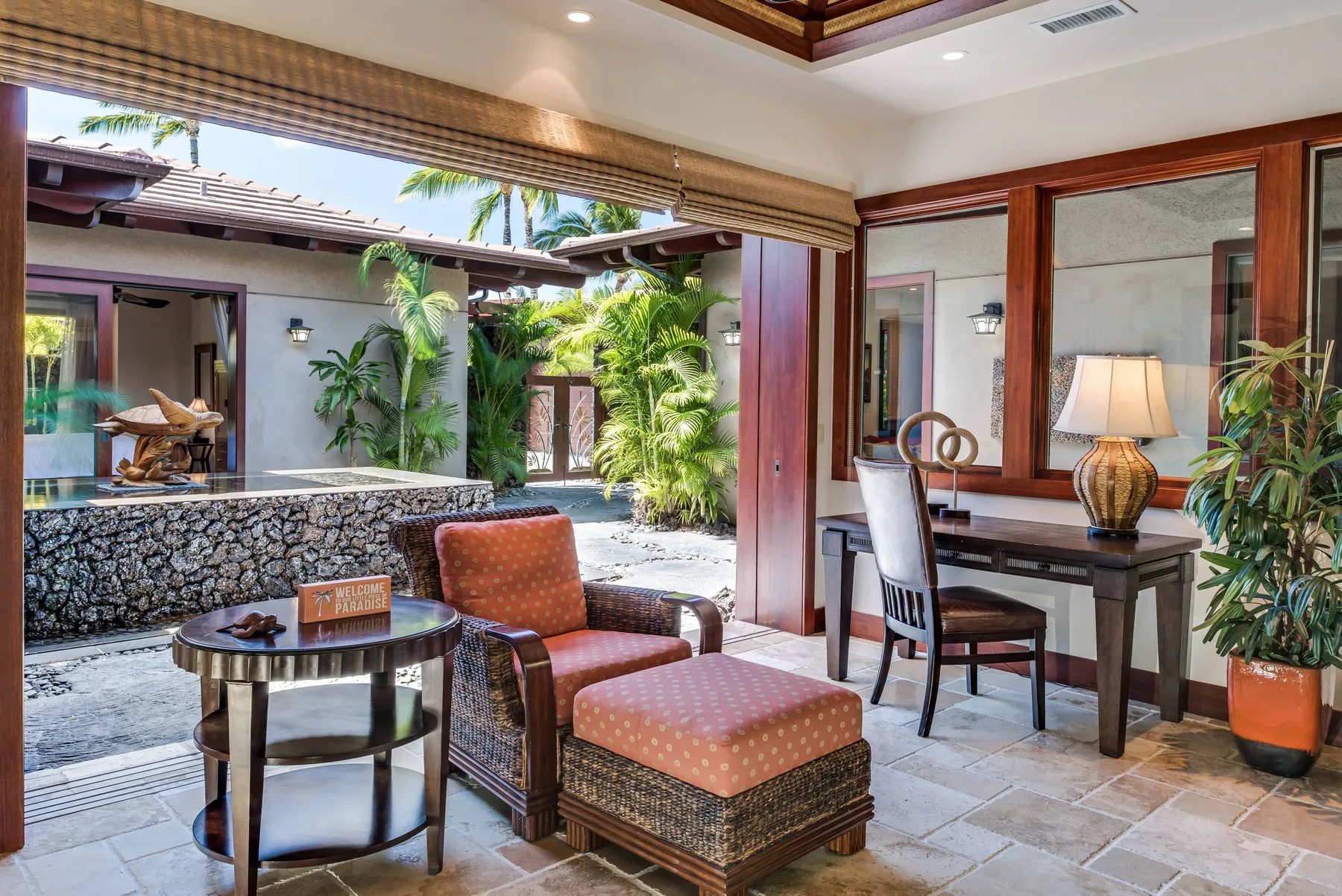 An open-air lounge with cushioned seating beside a dining table and tropical plants.
