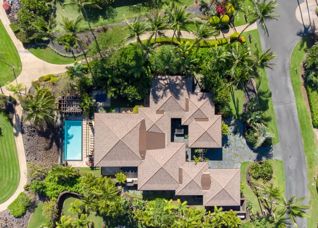 An aerial view of a house surrounded by landscaped gardens, with a swimming pool nearby.