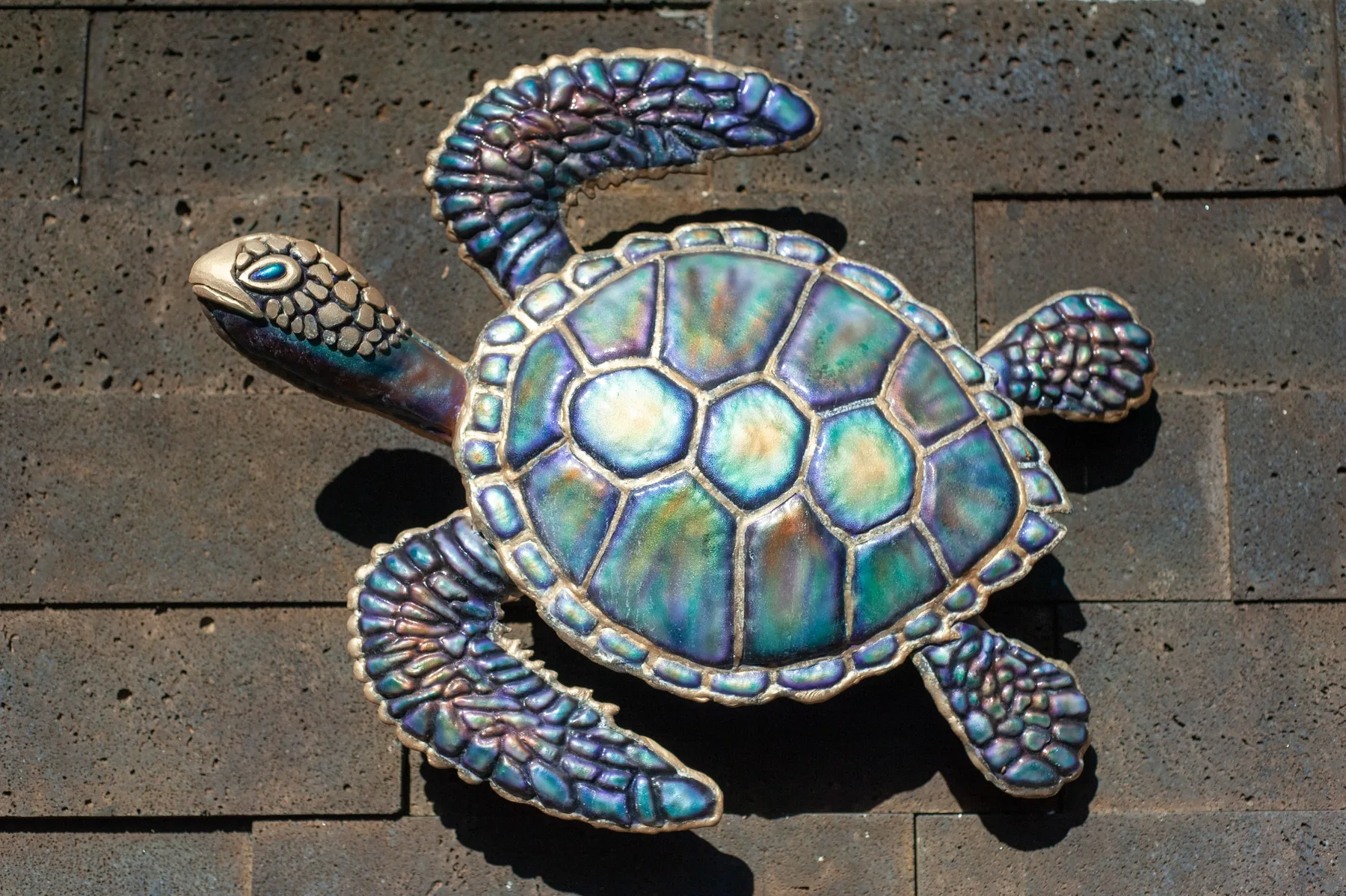 A decorative turtle sculpture with an iridescent shell rests on a paved surface.
