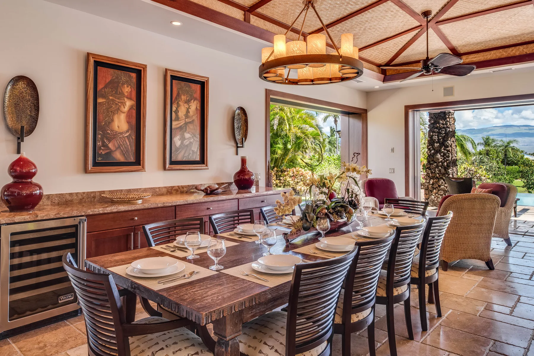 A dining room with a long wooden table and views of tropical greenery.