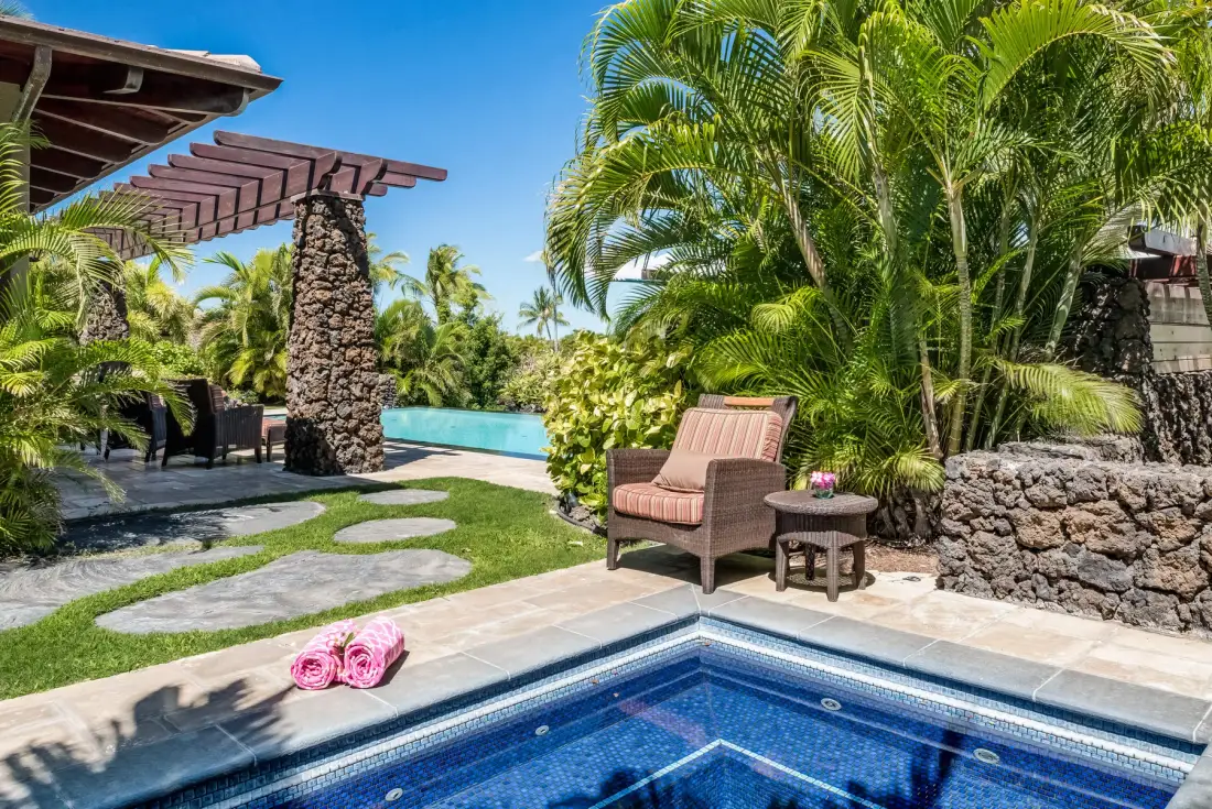 A tropical poolside patio with a lounge chair beside lush greenery.