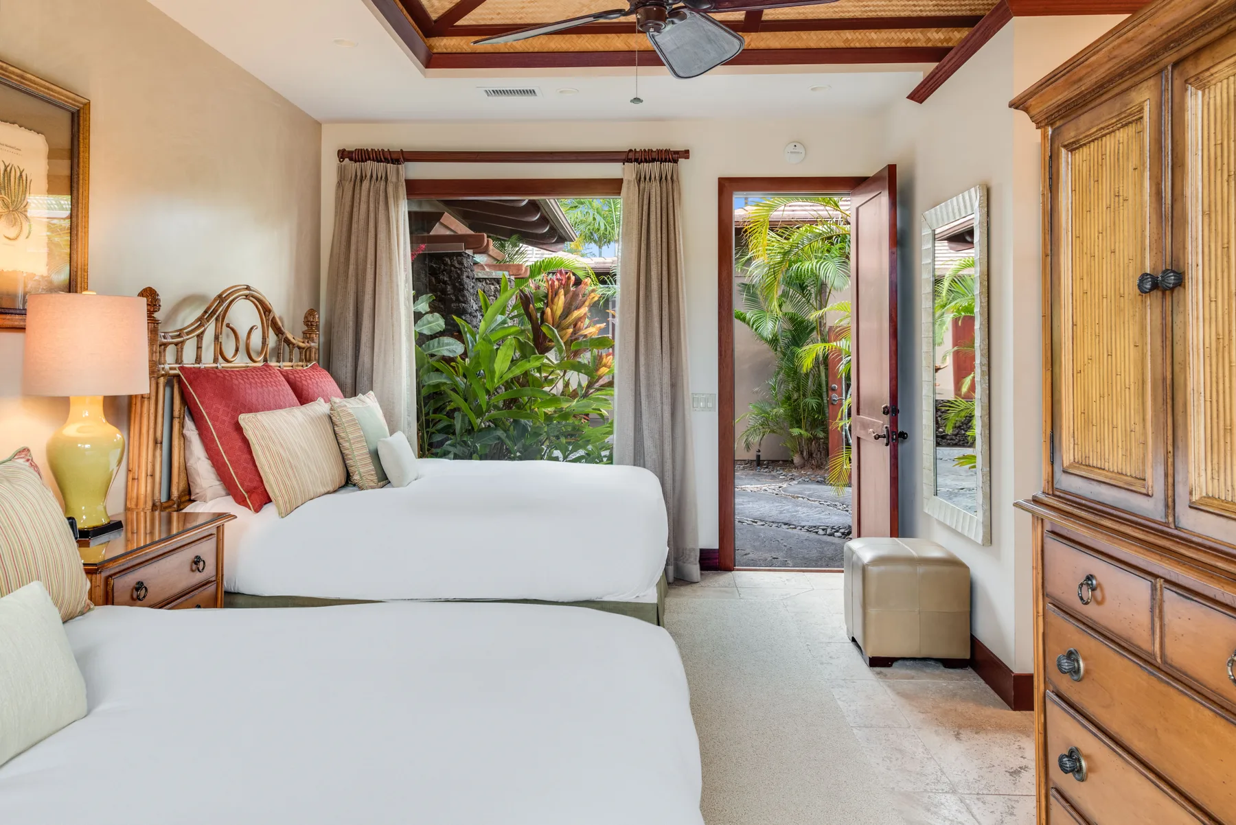 A bright bedroom with two beds, a bedside lamp, and garden views through open doors.