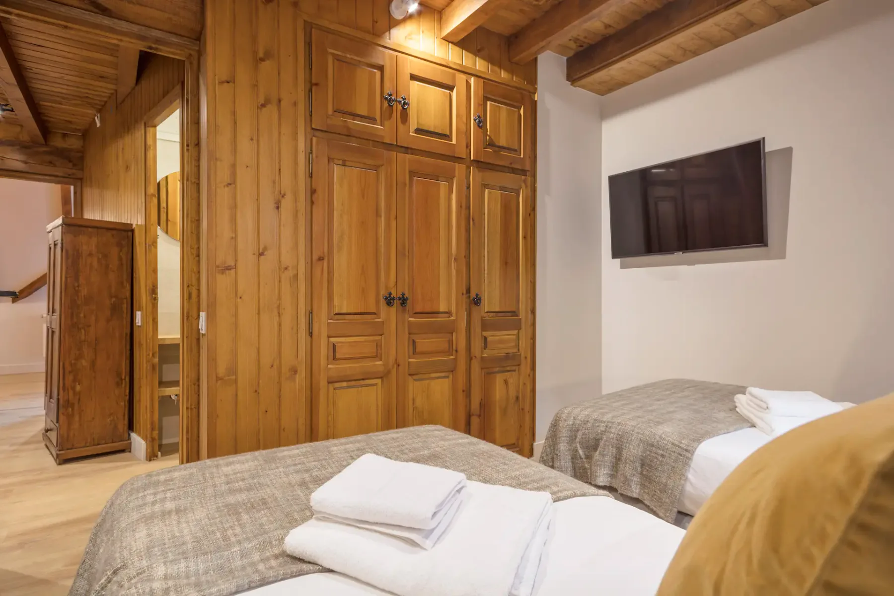 Bedroom with two single beds, folded white towels, and a wall-mounted television.