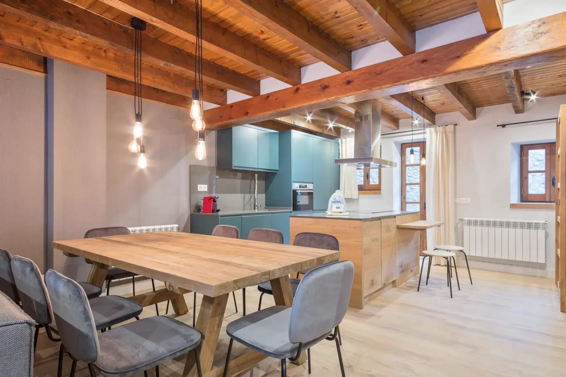 Open-plan kitchen and dining area with a wooden table beneath exposed ceiling beams.