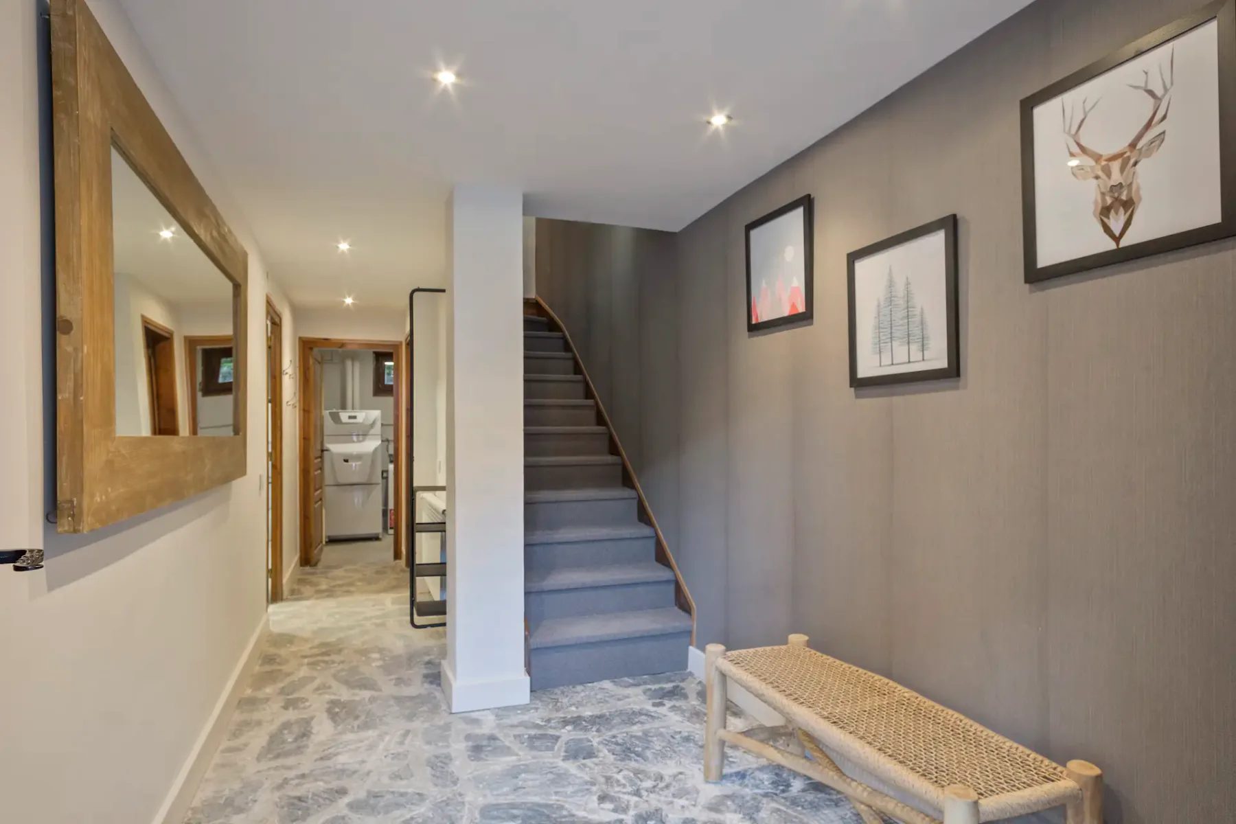 A hallway with a staircase, framed wall art, and a woven bench.