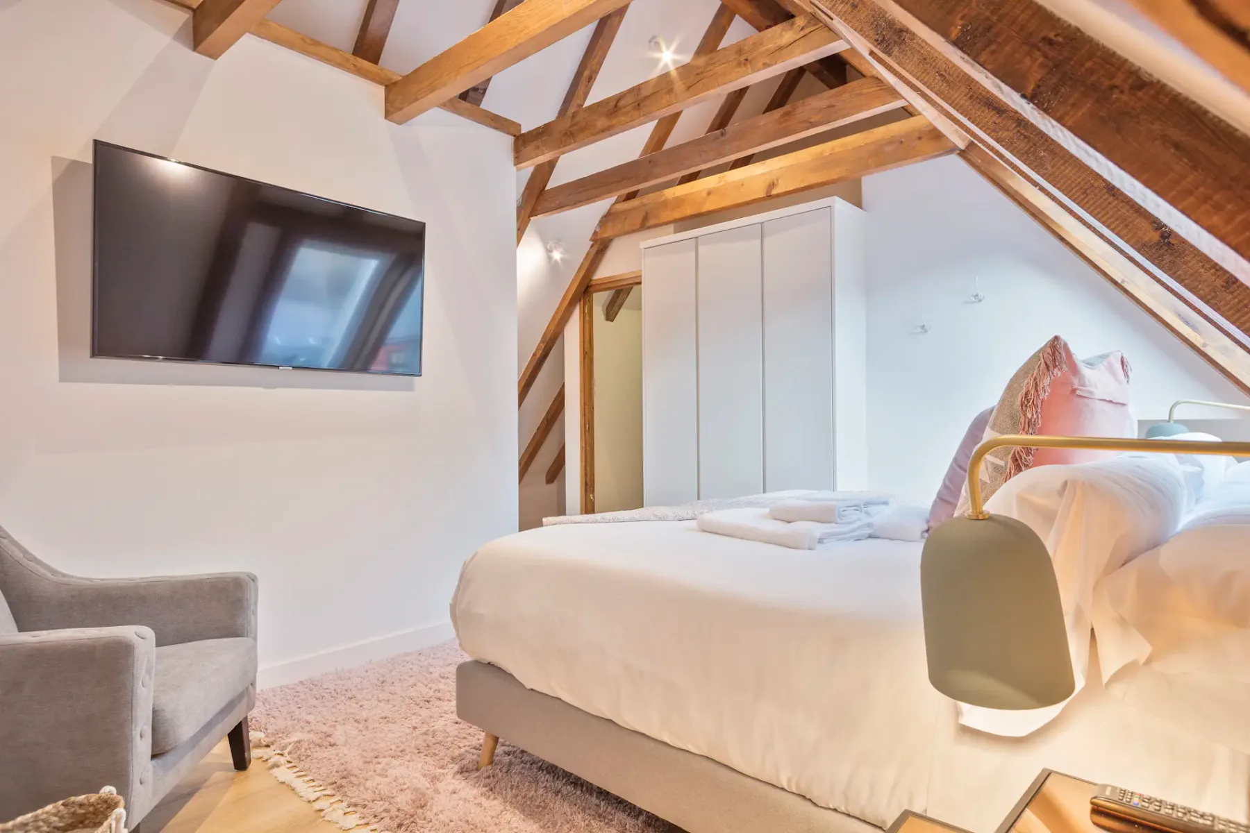 An attic bedroom with a bed, seating, and exposed wooden beams.