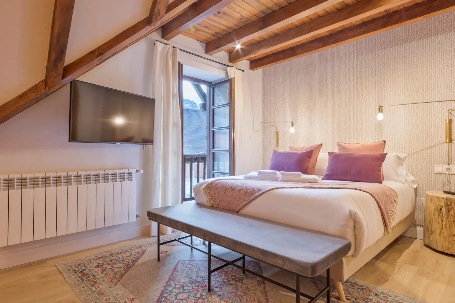 A bedroom with a bed, purple pillows, and a wooden-beam ceiling.