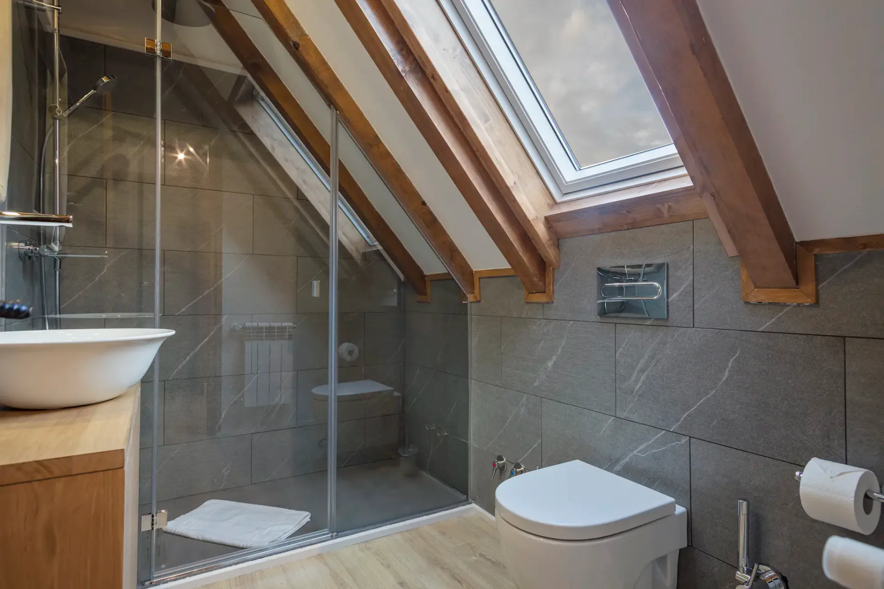 A sloped-ceiling bathroom with a glass shower, toilet, and skylight.