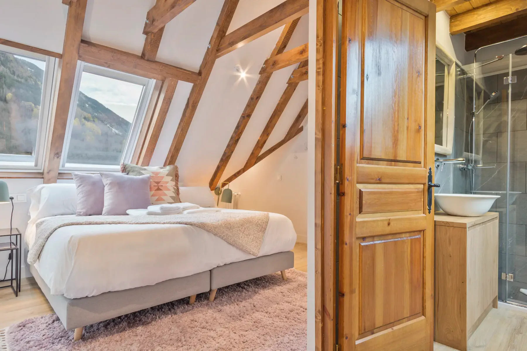 A sloped-ceiling bedroom with a bed and a bathroom visible through the open doorway.