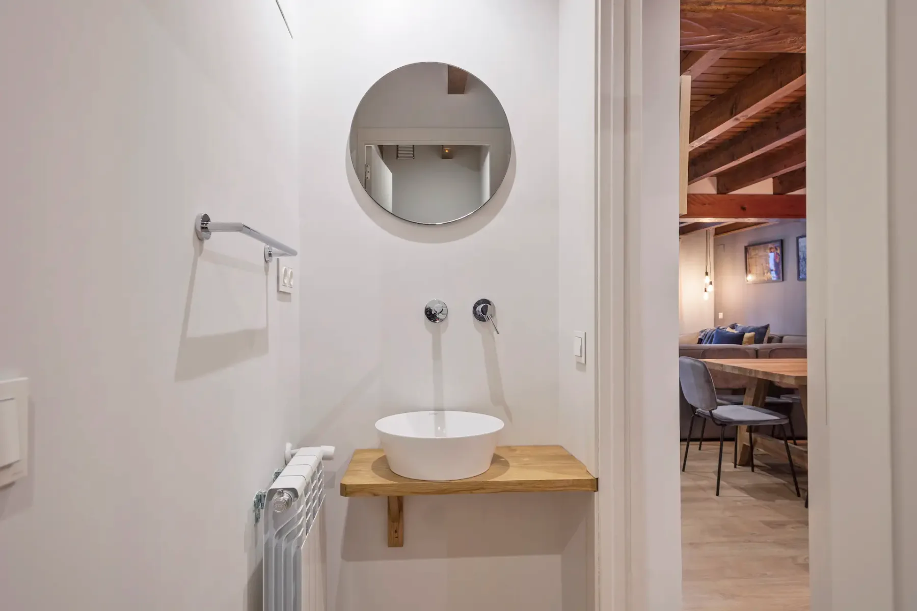 A washbasin area with a round mirror and an open doorway to a dining space.
