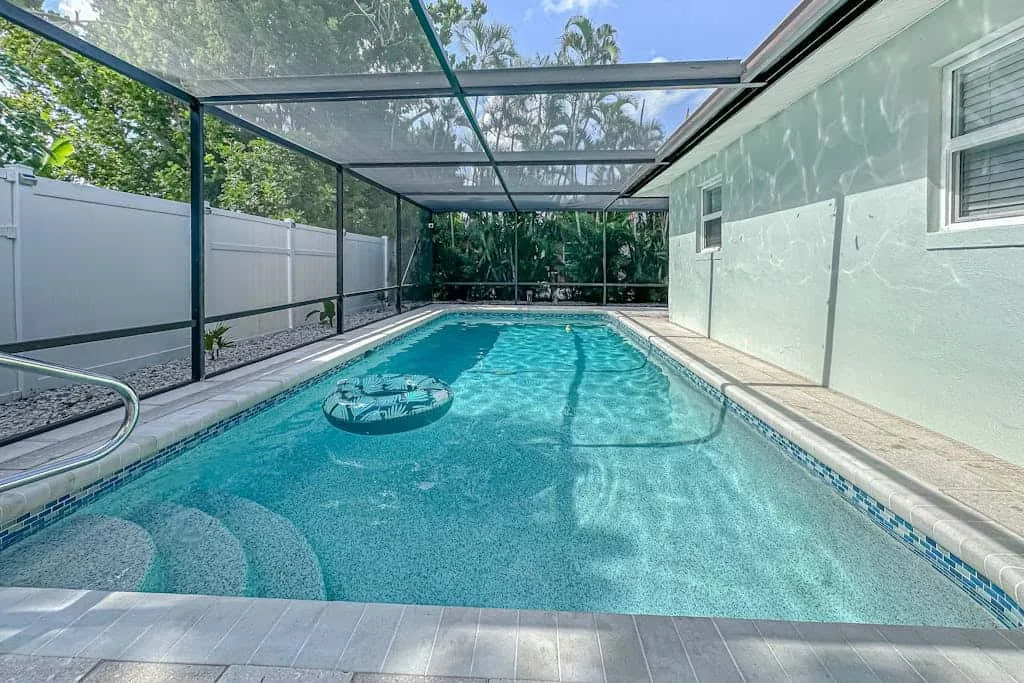 A swimming pool beneath a screened enclosure, with trees visible beyond it.