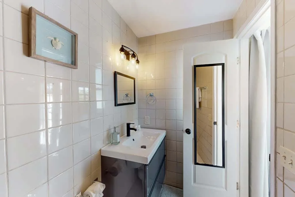 A tiled bathroom with a sink, wall mirror, and open doorway.