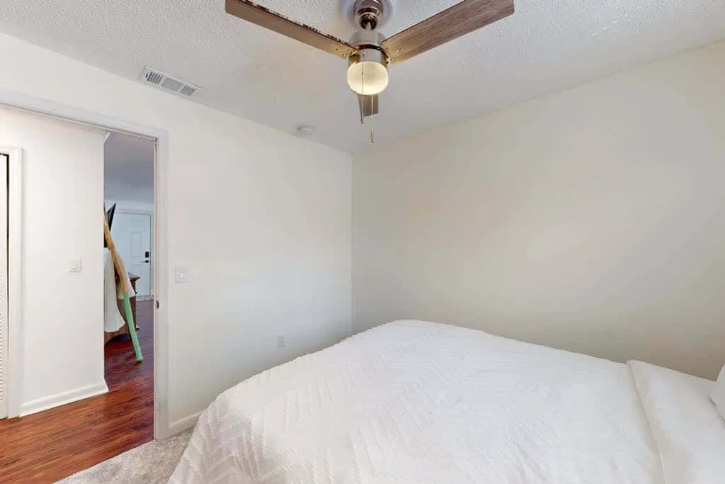 A bedroom with a white bed and a ceiling fan.
