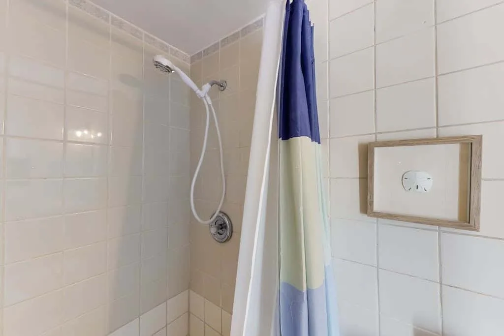 A tiled bathroom shower with a shower curtain and wall-mounted showerhead.