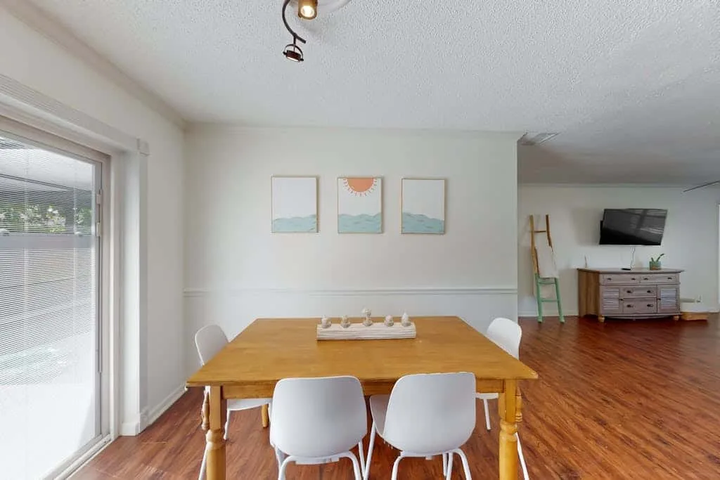 A dining area with a wooden table, white seating, and three framed prints.
