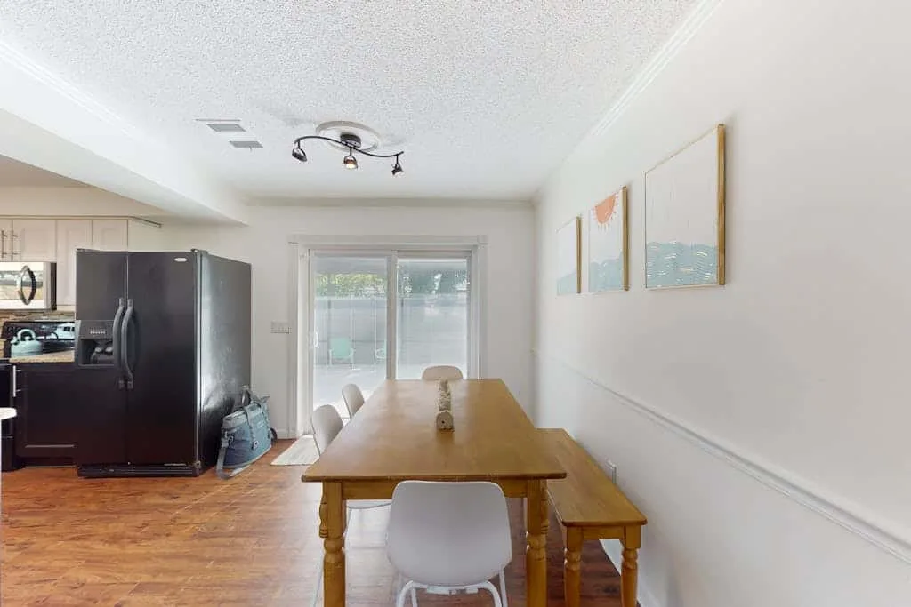 A dining area with a wooden table and seating beside a bright sliding glass door.