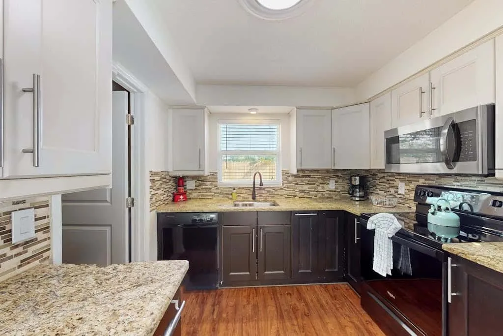 A kitchen with dark lower cabinets, light countertops, and a window above the sink.