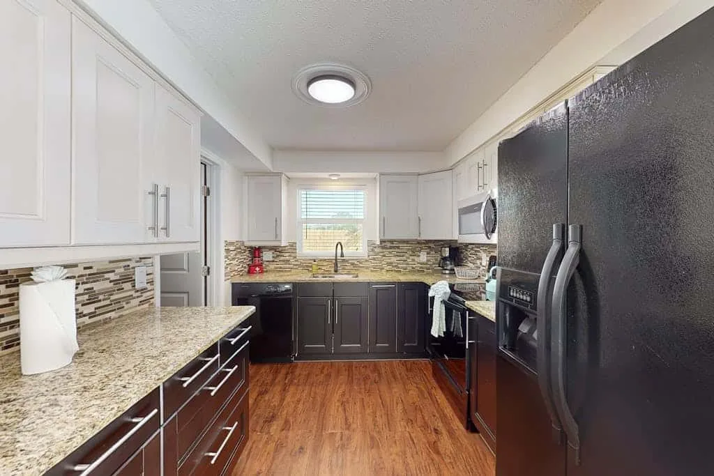 A kitchen with white cabinets, dark lower cabinets, and a refrigerator.