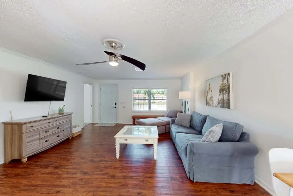 A living room with blue seating, a coffee table, and a wall-mounted television.