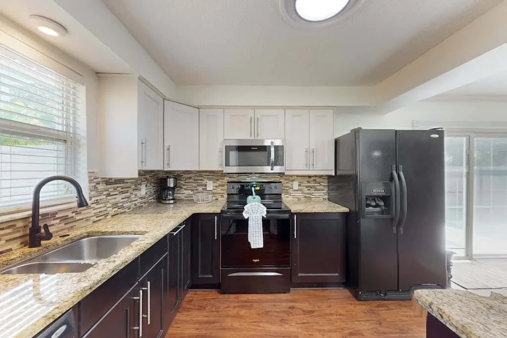 A kitchen with dark cabinets, light countertops, and stainless steel appliances.