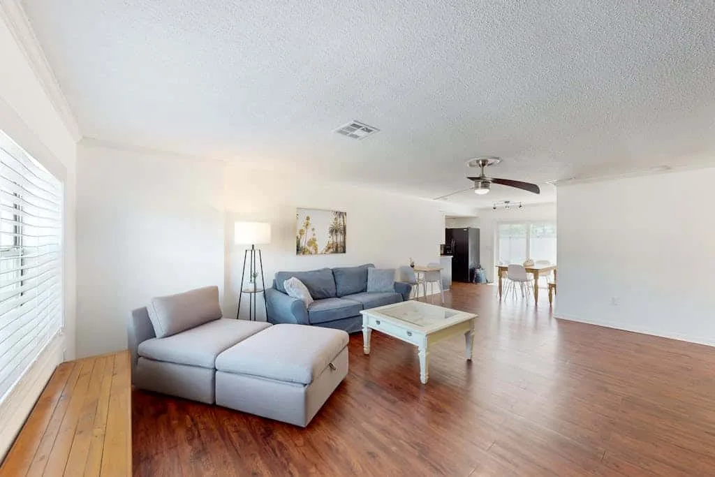 A bright living room with seating, a coffee table, and an open dining area.