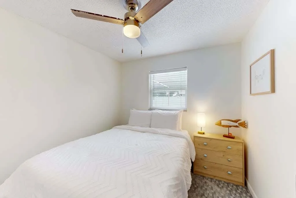 A bedroom with a bed, a window, and a wooden bedside dresser.