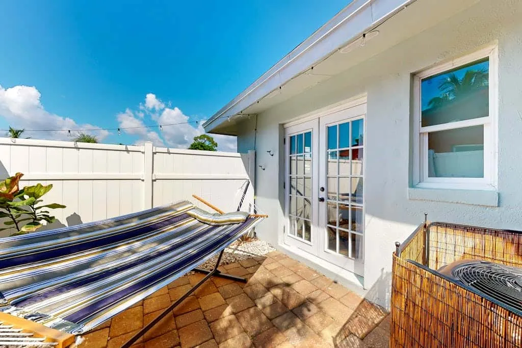 A sunlit patio with a striped hammock beside white walls and glass doors.