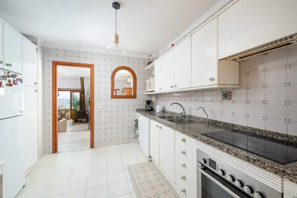 A bright kitchen with white cabinets, a countertop, and a built-in cooktop.