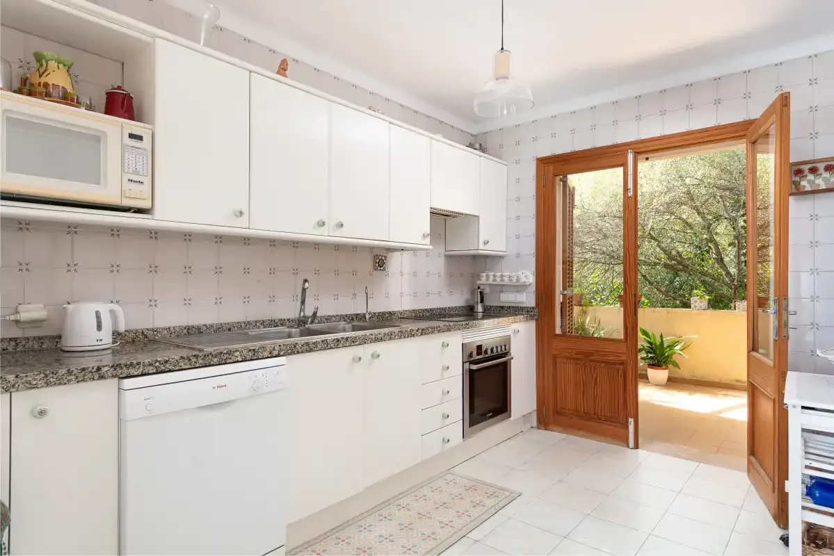 A bright kitchen with white cabinetry and an open wooden door to the patio.