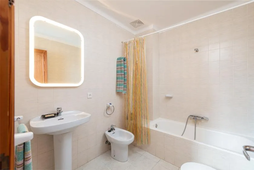 A tiled bathroom with a sink, bathtub, and colorful shower curtain.