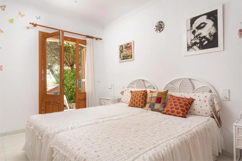 A bedroom with a large bed, patterned pillows, and an open wooden door to a garden.