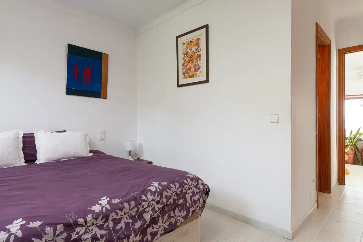 A bedroom with a bed covered in a purple floral bedspread.