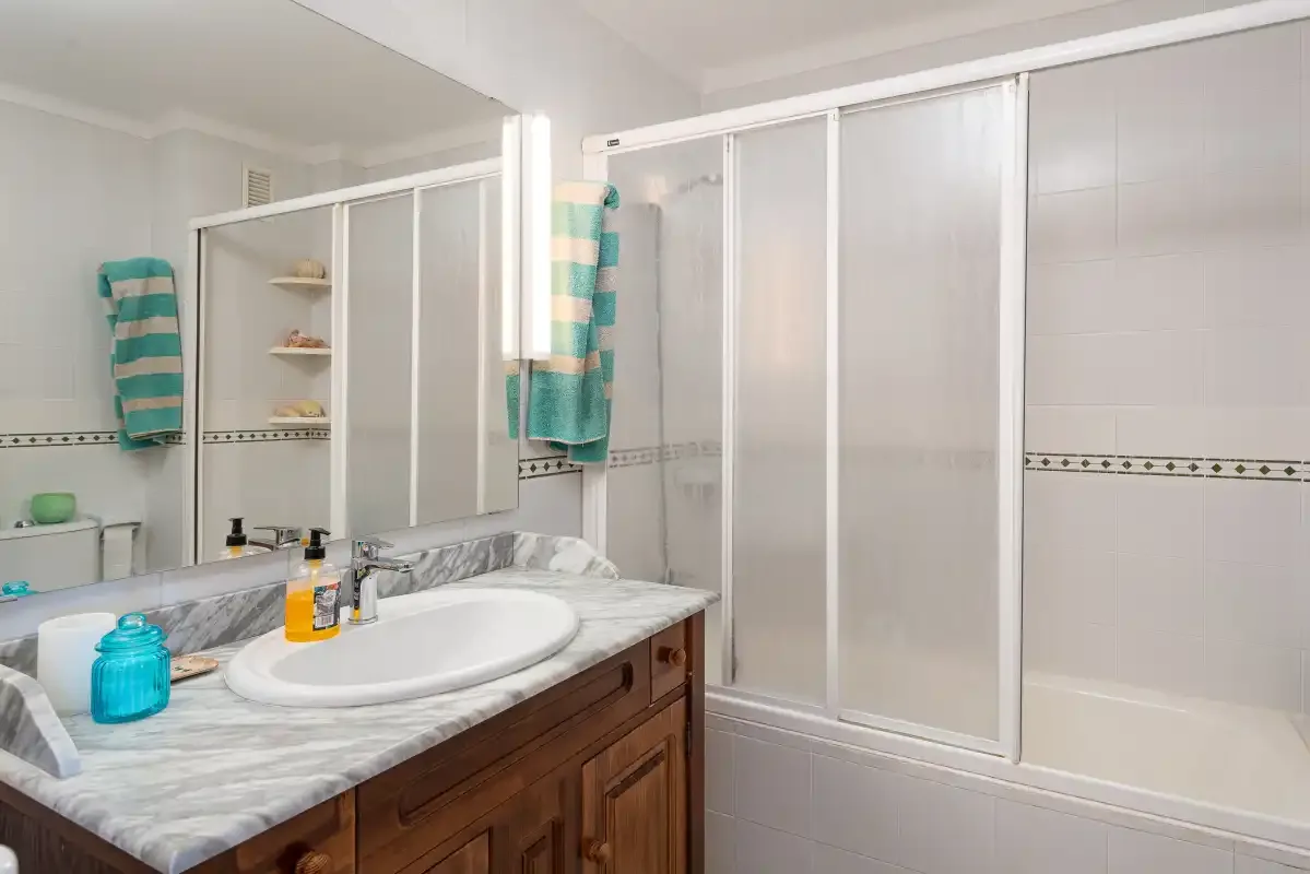 A bathroom with a sink, mirror, and shower.