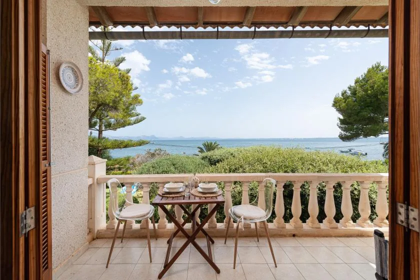A balcony with a small table and chairs overlooks the sea.