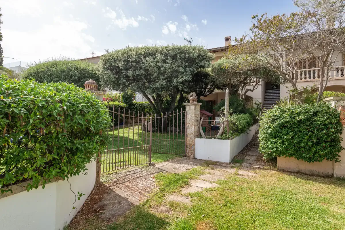 A garden entrance with a metal gate, shrubs, and a path leading to a house.