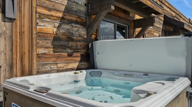 An outdoor hot tub sits beside a rustic wooden building.
