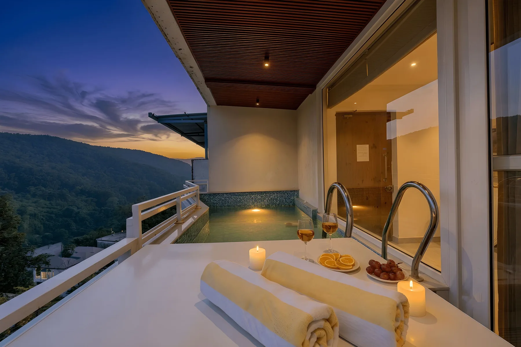 Una terraza junto a la piscina al aire libre da a un valle boscoso al anochecer.