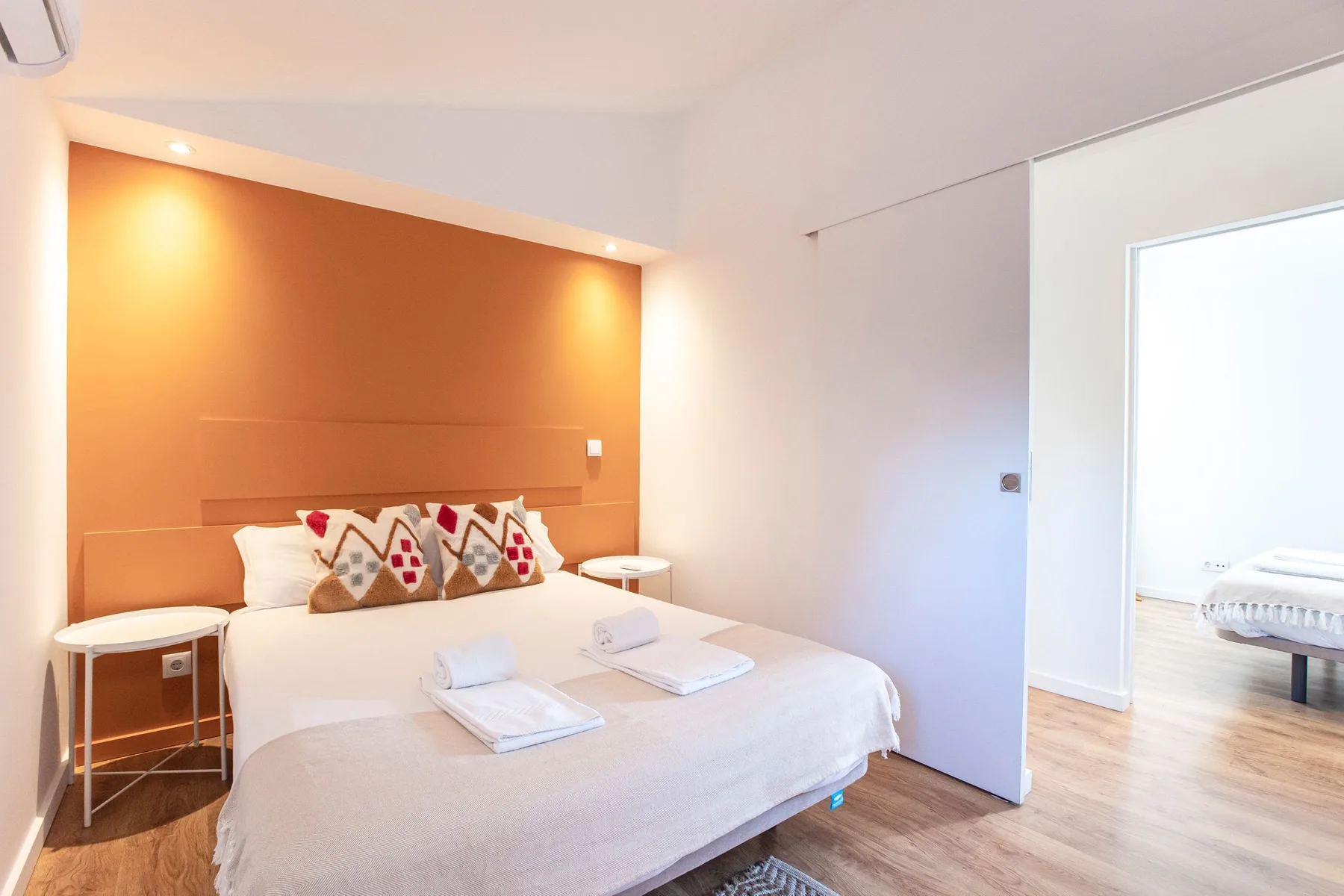 A bright bedroom with a bed set against an orange accent wall.