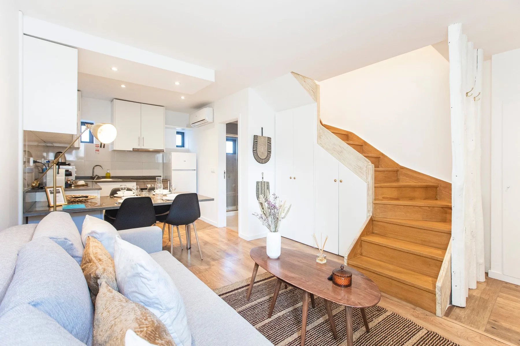 Open-plan living room with seating, a dining area, kitchen, and wooden staircase.