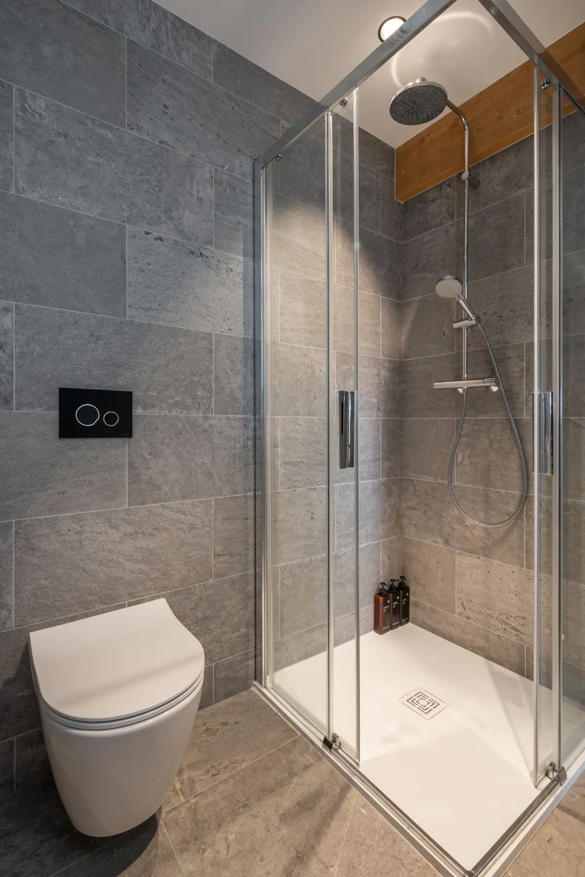 Modern bathroom with a wooden door, illuminated mirror, white rectangular sink, toiletries, heated towel rack, and stone tile walls.