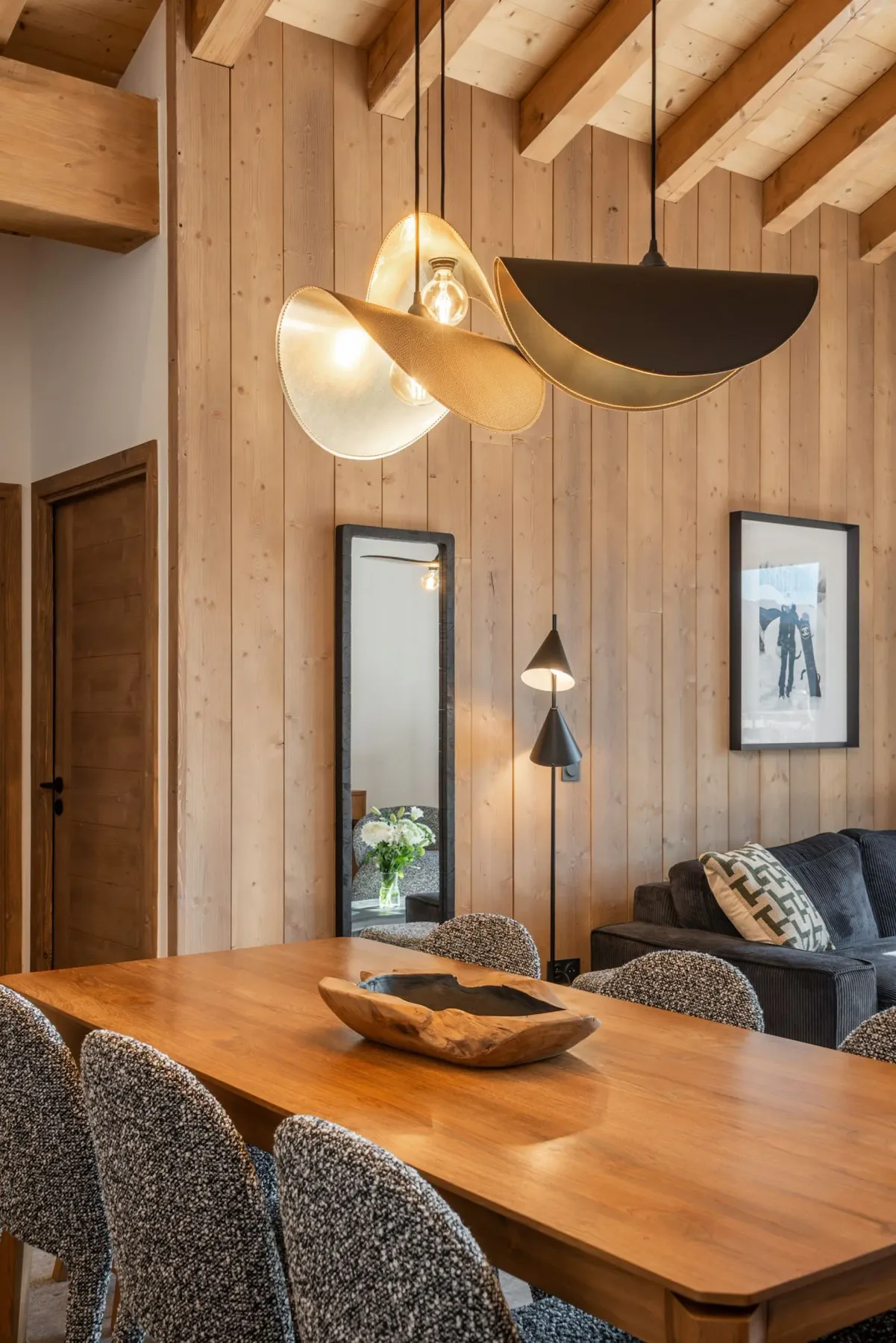 Modern kitchen with wooden ceiling, large wooden dining table, cushioned chairs, gray cabinets, and a unique pendant light.