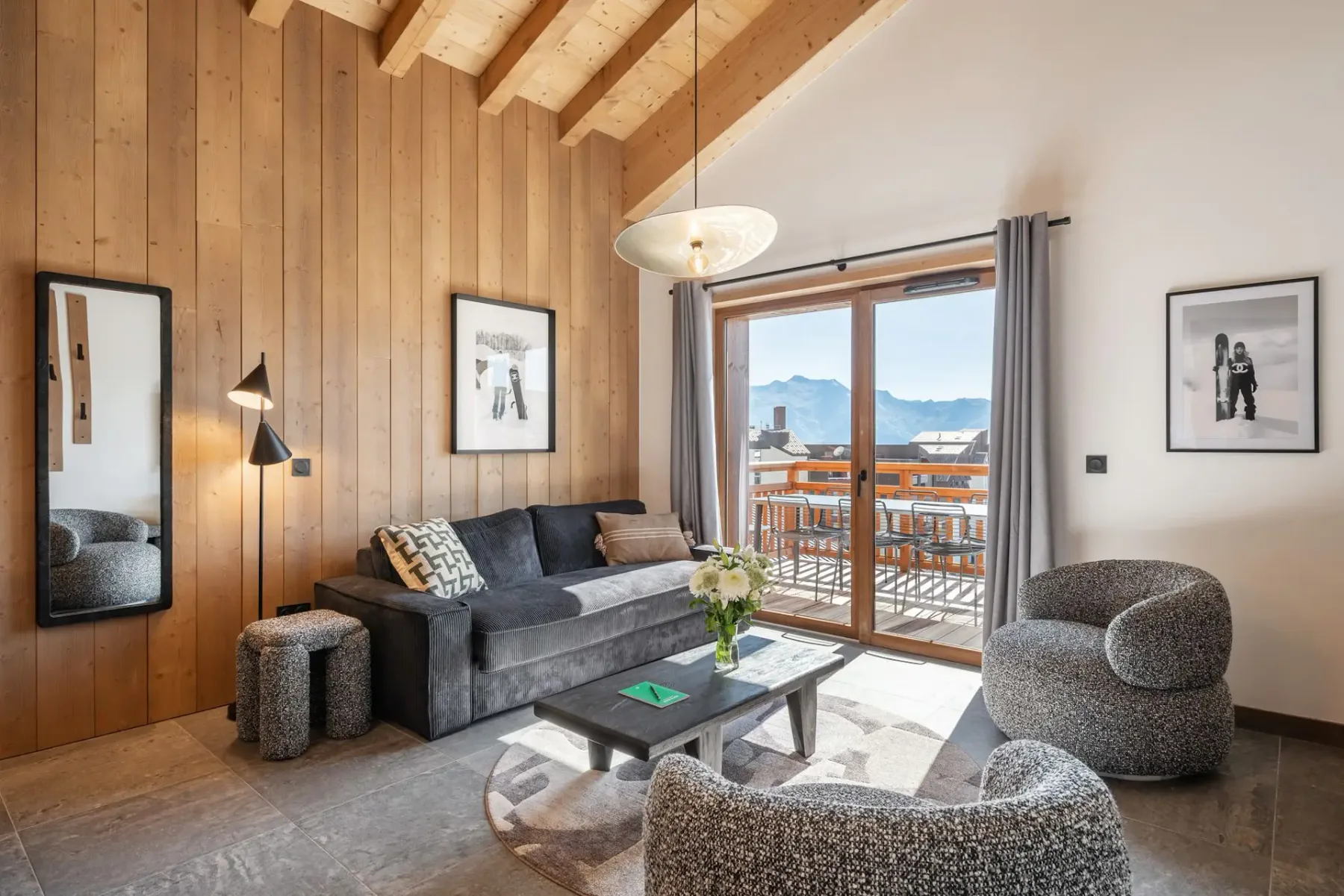 A cozy living room with wooden beams, modern furniture, a dining table, and large windows offering a mountain view.