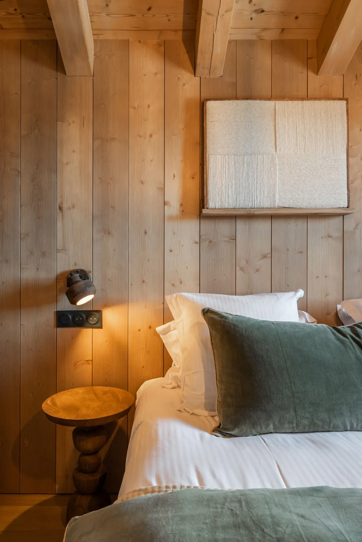 Cozy bedroom with wooden walls, a double bed with green accents, a window, modern lamp, and artwork on the wall.