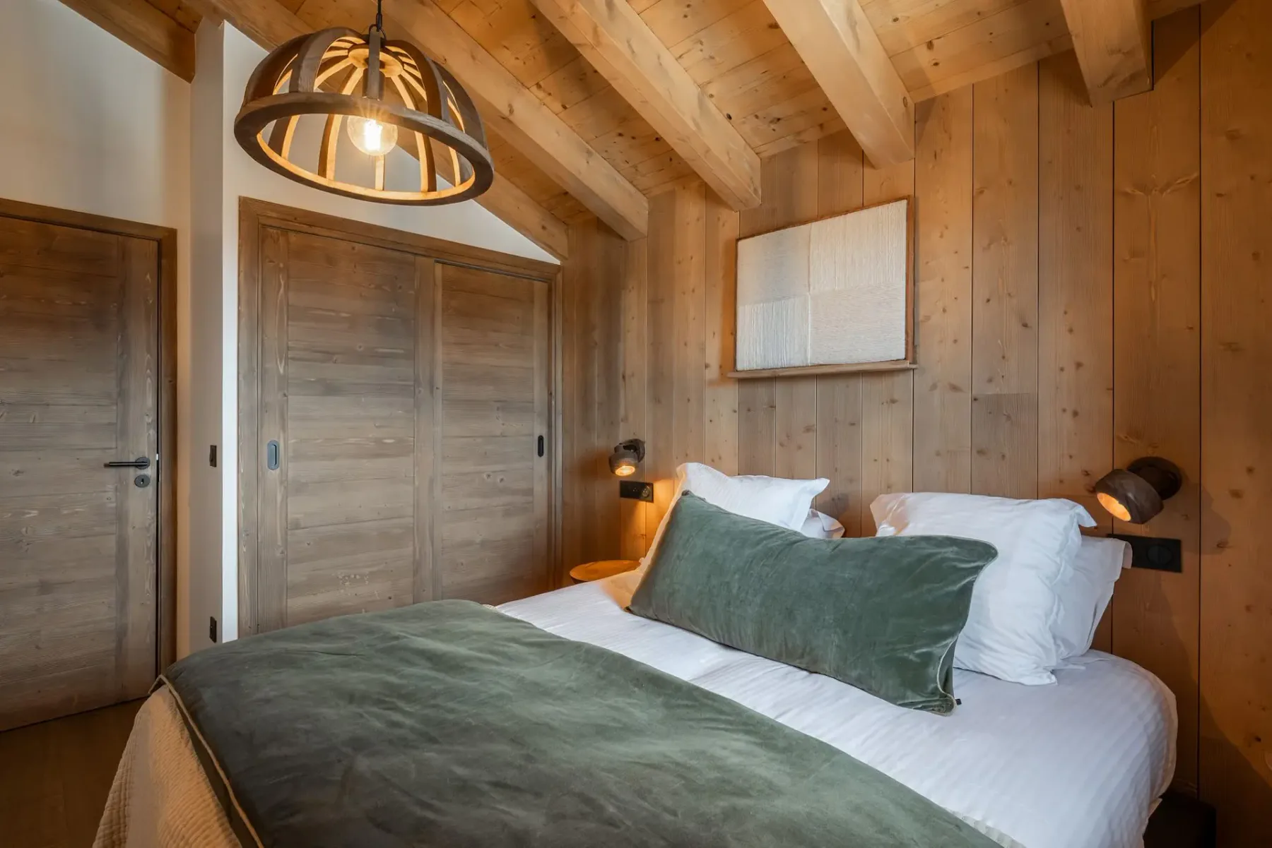 Cozy bedroom with wooden walls, a double bed with green accents, a window, modern lamp, and artwork on the wall.